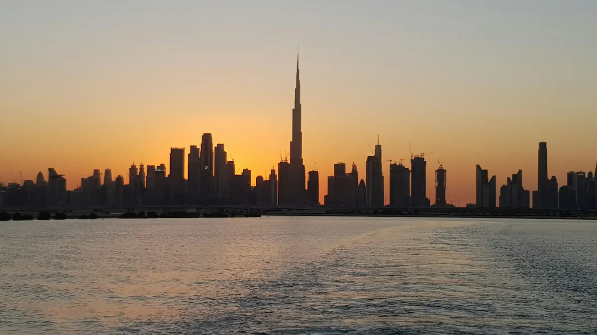The Dubai skyline at sunset across calm water